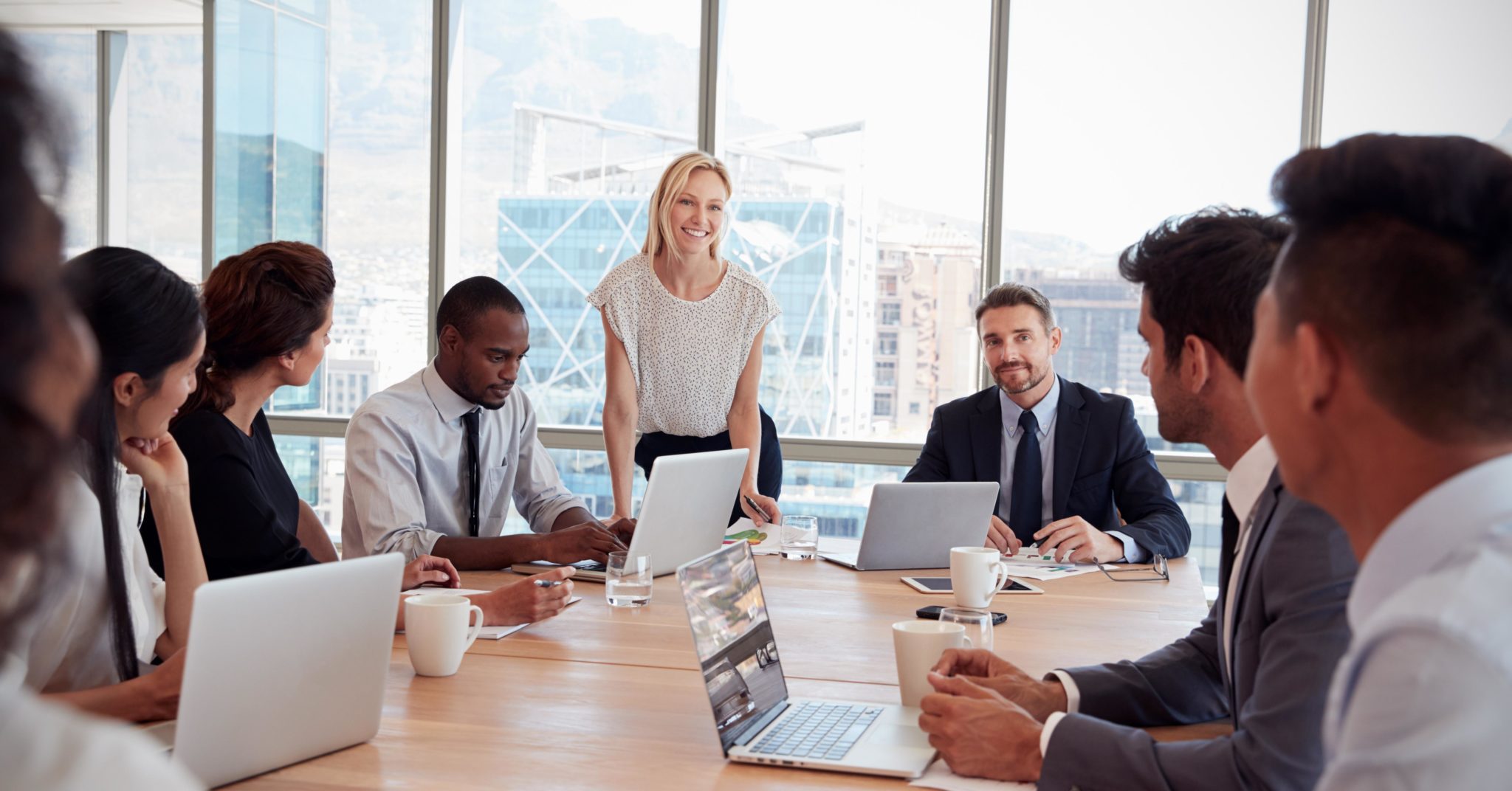 Image of woman standing at conference table presenting to a group of businessmen representing board diversity