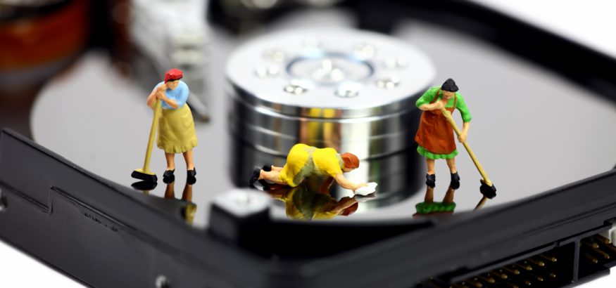 Three miniature maids in colorful outfits cleaning and mopping the surface of a computer hard drive. Representing sprucing up your marketing database.