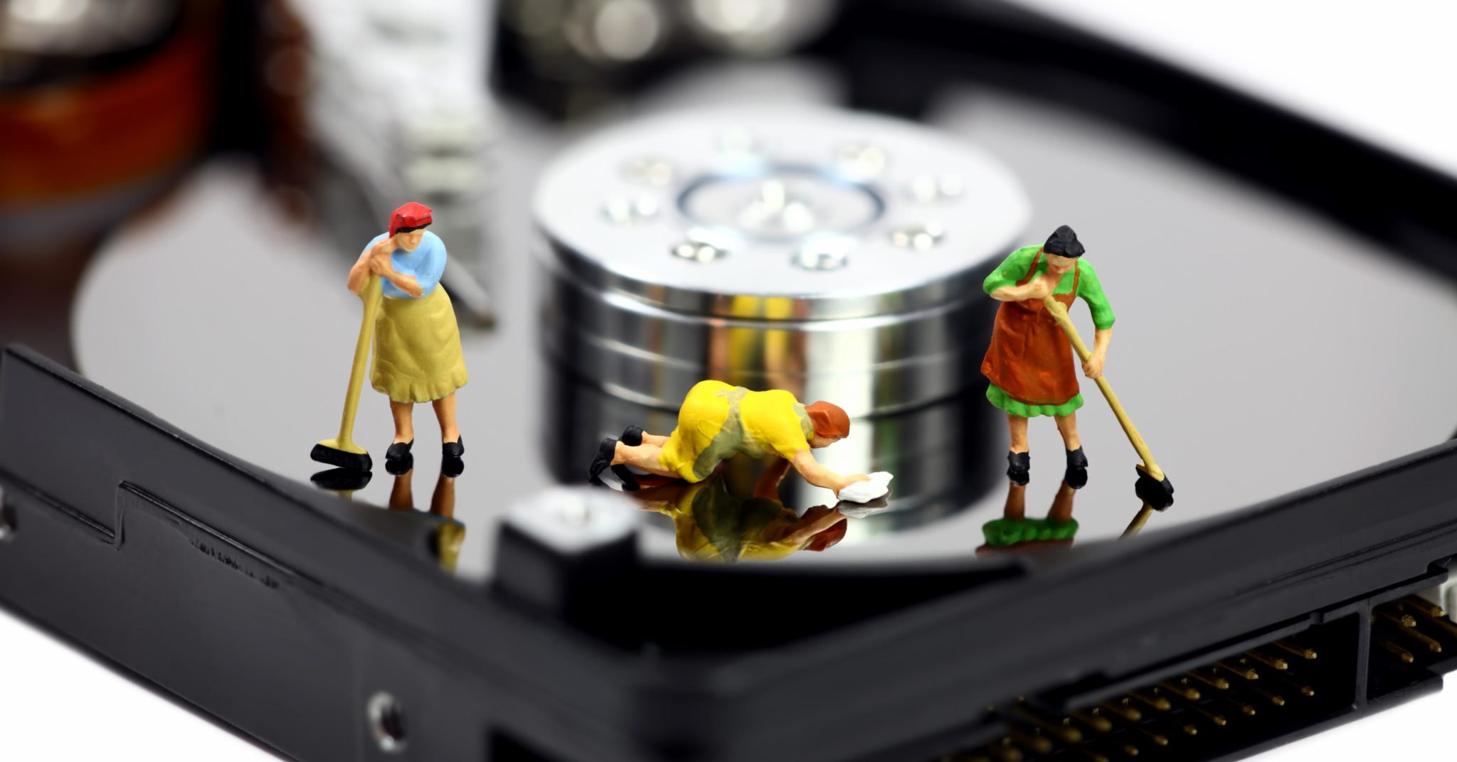 Three miniature maids in colorful outfits cleaning and mopping the surface of a computer hard drive. Representing sprucing up your marketing database.
